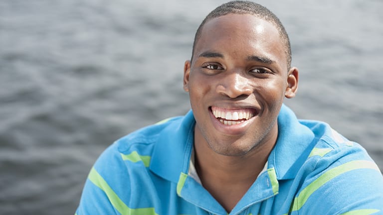 Smiling man wearing striped polo shirt with water in the background.