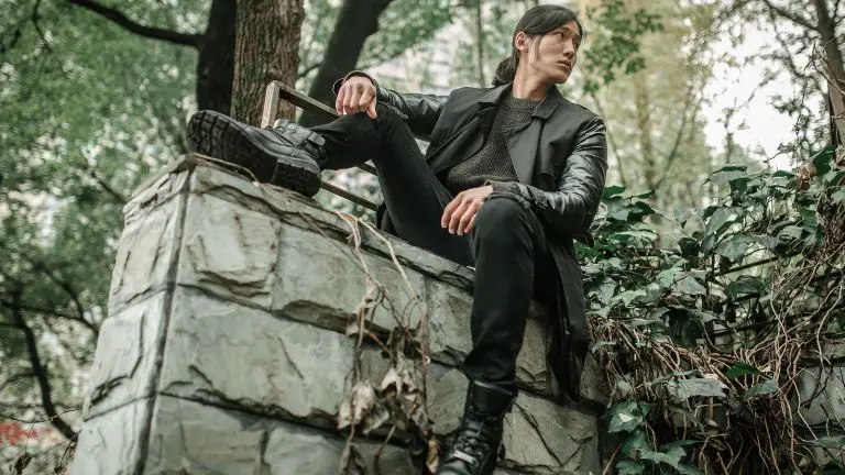 Man sitting on block wall wearing black jeans with black boots and black leather jacket.