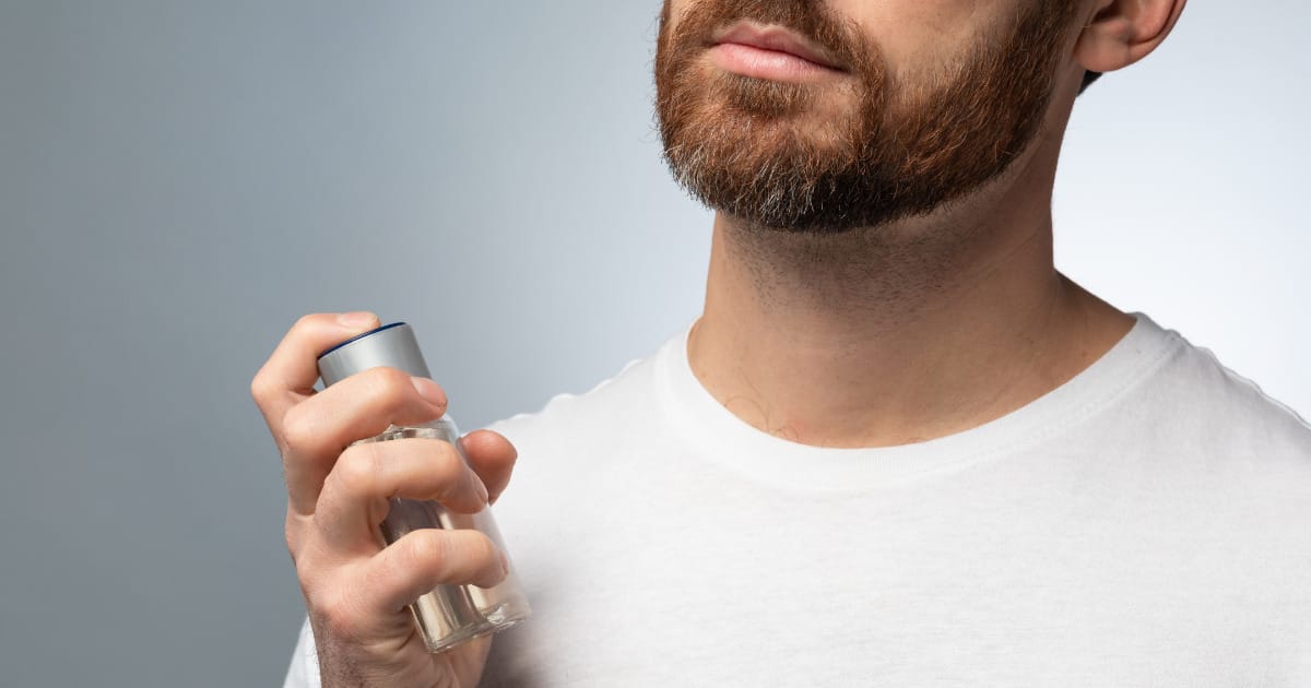 Man with beard sprays cologne on his neck.